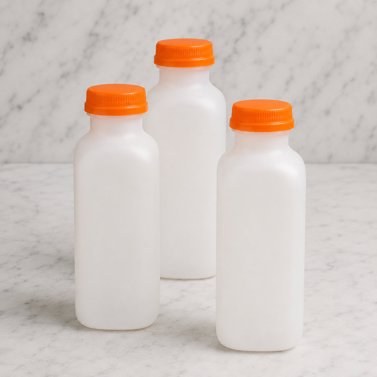 Three white bottles with orange lids on a marble surface